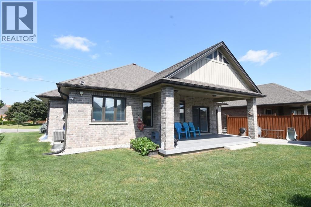 Rear exterior featuring a covered deck with stone pillars, a sliding glass patio door, a gabled roofline with vertical siding, and light-toned brickwork - 10 Craddock Boulevard, Jarvis, ON - Outdoor