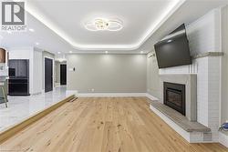 Open-concept living space with light wood-finish flooring, a contemporary fireplace with a stone mantel and hearth, recessed ceiling lighting, and a modern chandelier - 