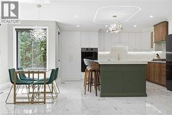 Modern kitchen featuring a contrasting green island, light wood-finish and white cabinetry, integrated appliances, and a built-in oven - 
