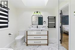 Bathroom featuring a white vanity with a marble-finish countertop and dark hardware, a freestanding toilet, a black wall-mounted towel warmer, a glass shower enclosure, and a skylight - 
