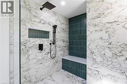 Walk-in shower featuring full-height marble-patterned tile, a dark green accent tile wall, a built-in bench, matte black fixtures, and a glass enclosure - 
