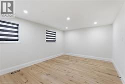 Spacious room featuring light wood-finish flooring, recessed lighting, and two windows with zebra blinds - 