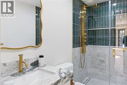 Modern bathroom featuring a walk-in shower with glass enclosure, gold-finish shower system, and dark green subway tile - 