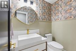 Powder room featuring floral wallpaper, wainscoting, a gold-framed mirror, a rectangular vessel sink with a gold-tone faucet, and a contemporary toilet - 