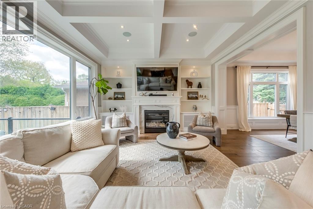 Spacious living area featuring a coffered ceiling, large picture windows, a built-in fireplace with a mantel, integrated shelving, and hardwood-finish flooring - 436 Willis Drive, Oakville, ON - Indoor Photo Showing Living Room With Fireplace