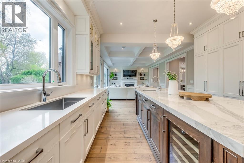Gourmet kitchen featuring a large central island with integrated beverage refrigerator, white perimeter cabinetry with under-cabinet lighting, stainless steel undermount sink with gooseneck faucet, an - 436 Willis Drive, Oakville, ON - Indoor Photo Showing Kitchen With Upgraded Kitchen