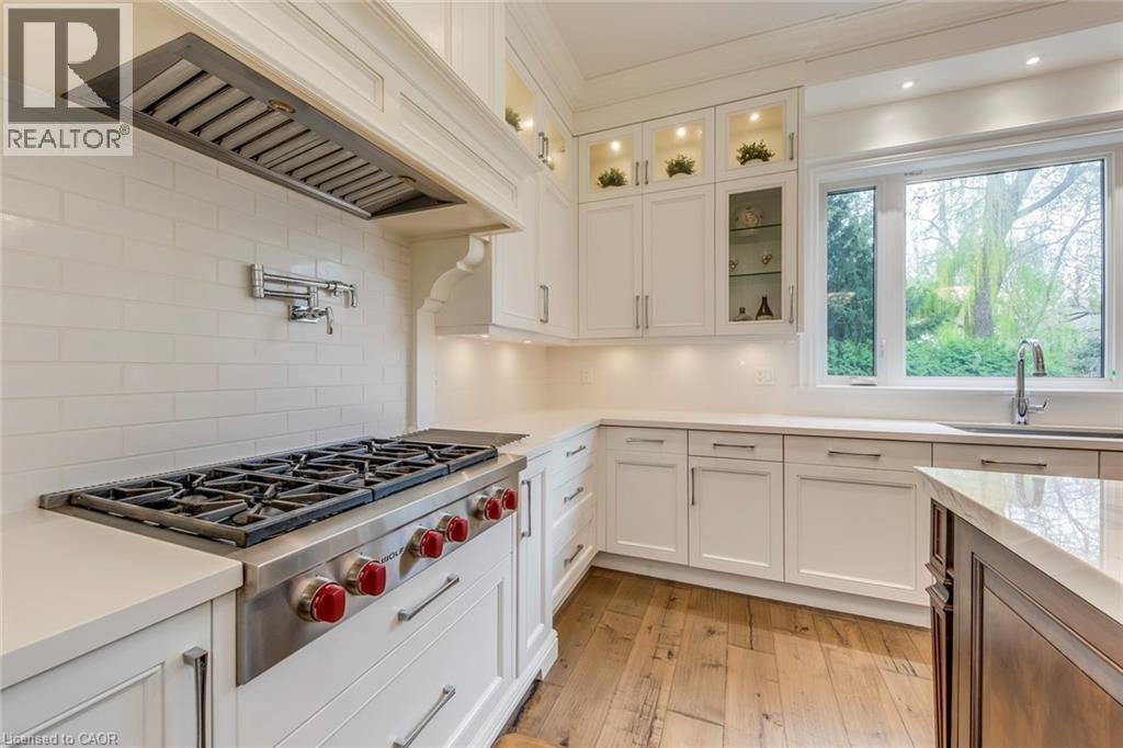 Gourmet kitchen featuring a professional-grade gas range, pot filler, recessed lighting, white cabinetry with display uppers, and wood-finish flooring - 436 Willis Drive, Oakville, ON - Indoor Photo Showing Kitchen With Upgraded Kitchen