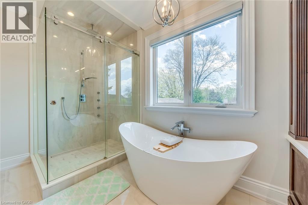 Freestanding soaking tub with chrome fixtures, large window with exterior views, glass-enclosed shower with multiple shower heads, recessed lighting, and crown molding - 436 Willis Drive, Oakville, ON - Indoor Photo Showing Bathroom