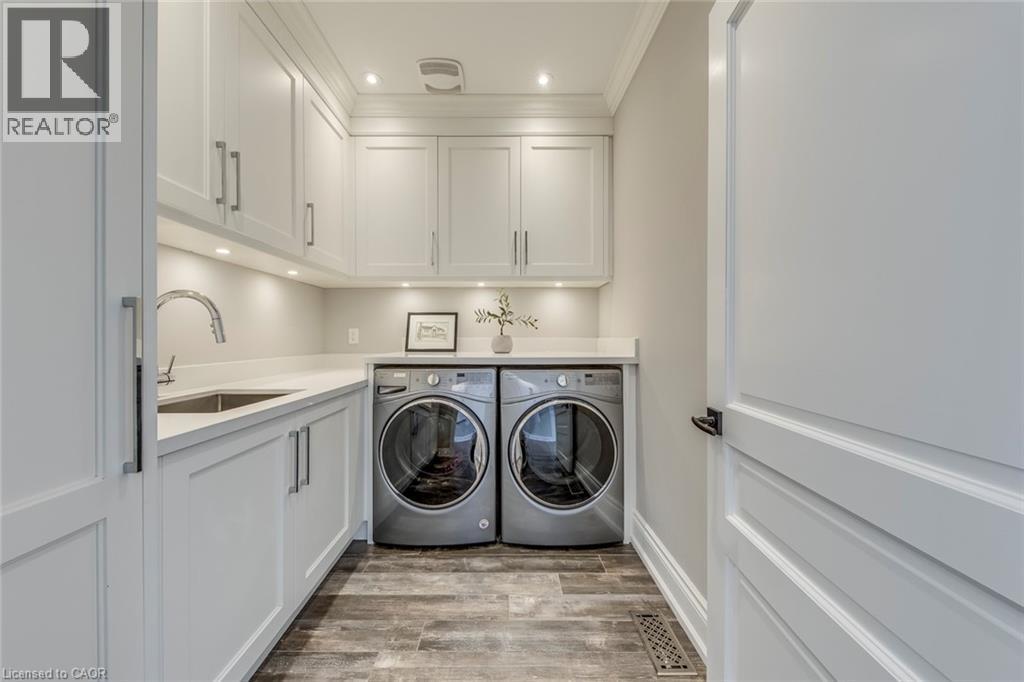 Laundry area featuring white shaker-style cabinetry with chrome hardware, an undermount sink with a gooseneck faucet, light-toned countertops, and wood-finish flooring - 436 Willis Drive, Oakville, ON - Indoor Photo Showing Laundry Room