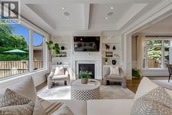 Sophisticated living room showcasing a coffered ceiling with recessed lighting, a linear gas fireplace with built-in shelving, and hardwood flooring - 