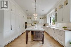 Gourmet kitchen featuring a substantial island with stone countertop, extensive white cabinetry, light wood-finish flooring, recessed lighting, and a multi-tiered chandelier - 