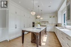 Spacious kitchen featuring white cabinetry, wood-finish flooring, a center island with a marble countertop, and built-in appliances - 