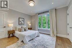 Serene primary bedroom showcasing hardwood flooring, soft neutral wall finishes, and abundant natural light from multi-panel glass doors opening to lush outdoor greenery - 