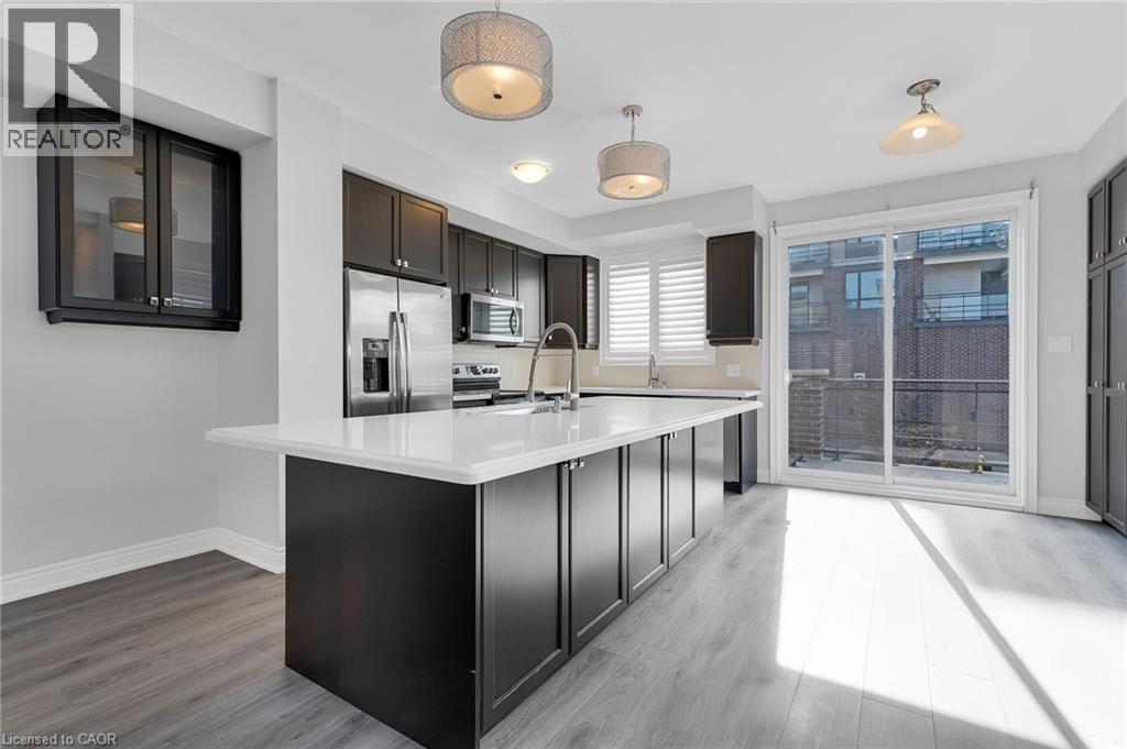Modern kitchen featuring a large central island with a white countertop, dark flat-panel cabinetry, stainless steel appliances, and light wood-finish flooring - 2 Waterview Lane, Grimsby, ON - Indoor Photo Showing Kitchen With Upgraded Kitchen