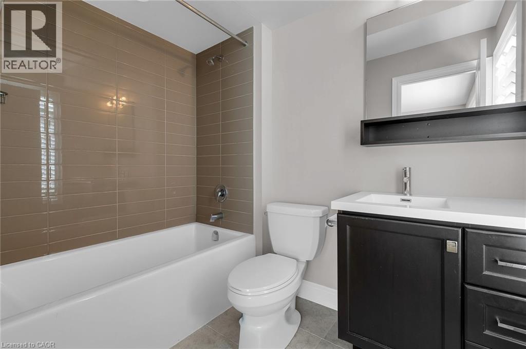 Bathroom featuring a white bathtub with subway tile surround, polished chrome fixtures, a dark wood-finish vanity with an integrated sink, and a framed mirror - 2 Waterview Lane, Grimsby, ON - Indoor Photo Showing Bathroom