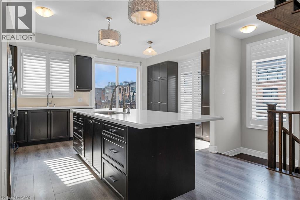 Kitchen featuring a large island with an integrated sink, dark wood-finish cabinetry, light-toned countertops, wood-finish flooring, and a sliding glass door - 2 Waterview Lane, Grimsby, ON - Indoor Photo Showing Kitchen