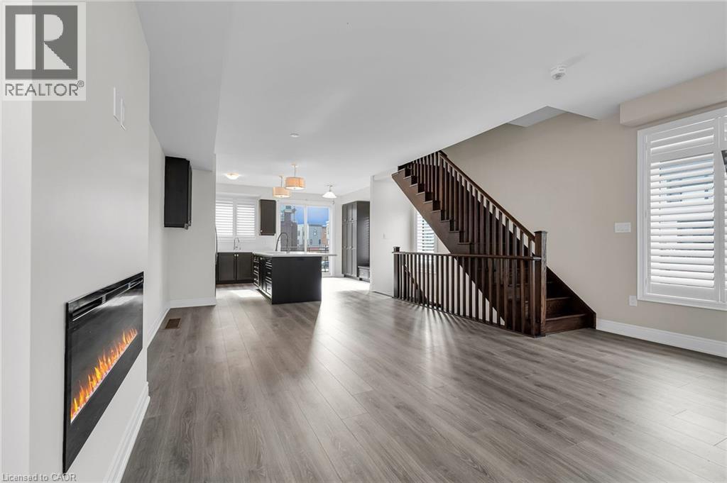 Open concept living space featuring wood-finish flooring, a contemporary electric fireplace, and a dark wood staircase with matching railing - 2 Waterview Lane, Grimsby, ON - Indoor Photo Showing Living Room With Fireplace