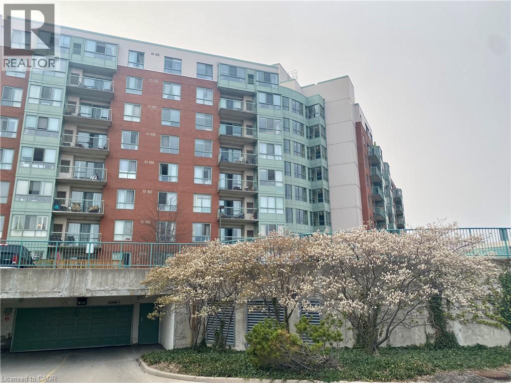 Multi-story residential building featuring brick and light green paneling, individual balconies with glass railings, and a ground-level parking garage with a green door - 30 Blue Springs Drive Unit# Ph3, Waterloo, ON - Outdoor With Balcony With Facade