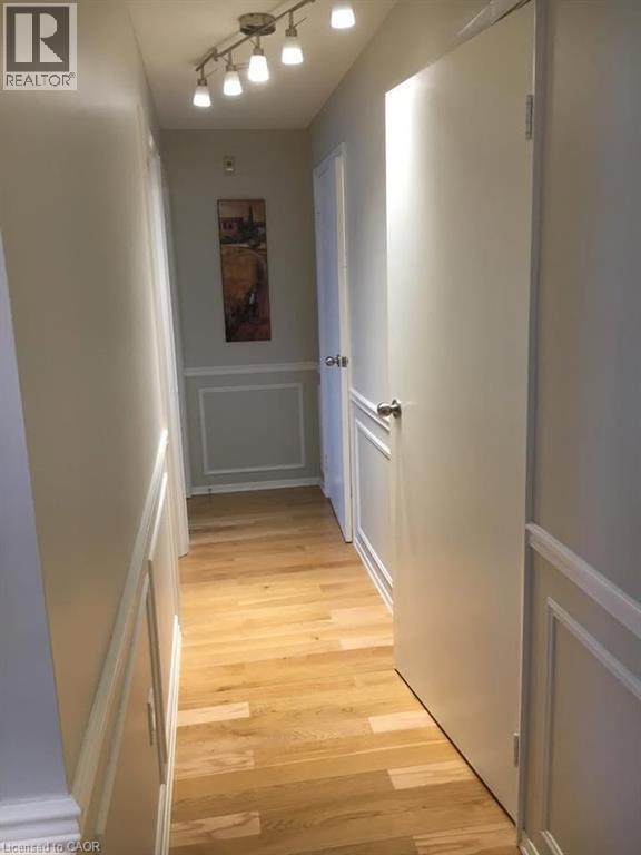 Hardwood flooring throughout a hallway featuring track lighting, white paneled wall molding, and neutral wall tones - 30 Blue Springs Drive Unit# Ph3, Waterloo, ON - Indoor Photo Showing Other Room
