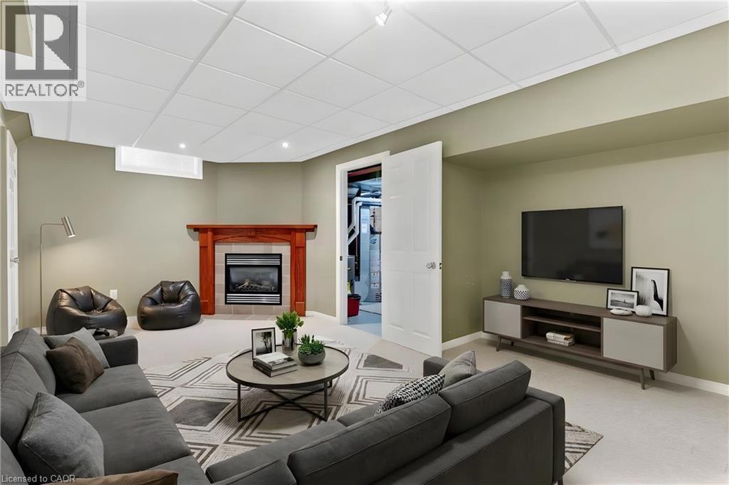Finished lower level featuring a fireplace with a wood-finish mantel and stone surround, recessed lighting, drop ceiling, and neutral carpeting - 129 Kovac Road, Cambridge, ON - Indoor