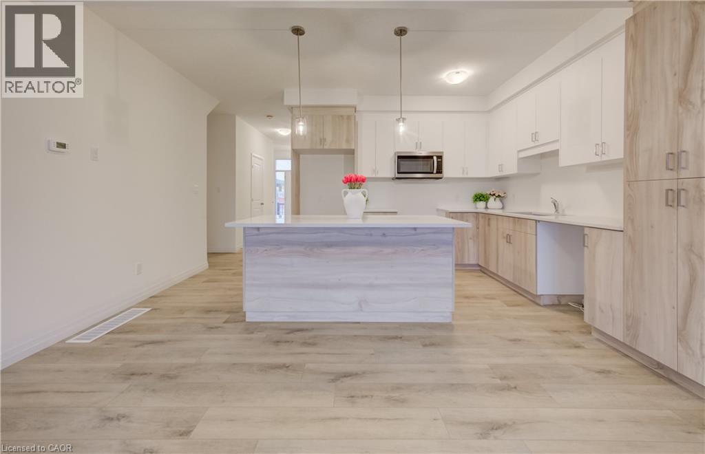 Modern kitchen featuring a spacious open floor plan with a substantial waterfall-edge island, white cabinetry, wood-finish flooring throughout, stainless steel appliances including a built-in microwav - 89 Rivergreen Crescent, Cambridge, ON - Indoor Photo Showing Kitchen