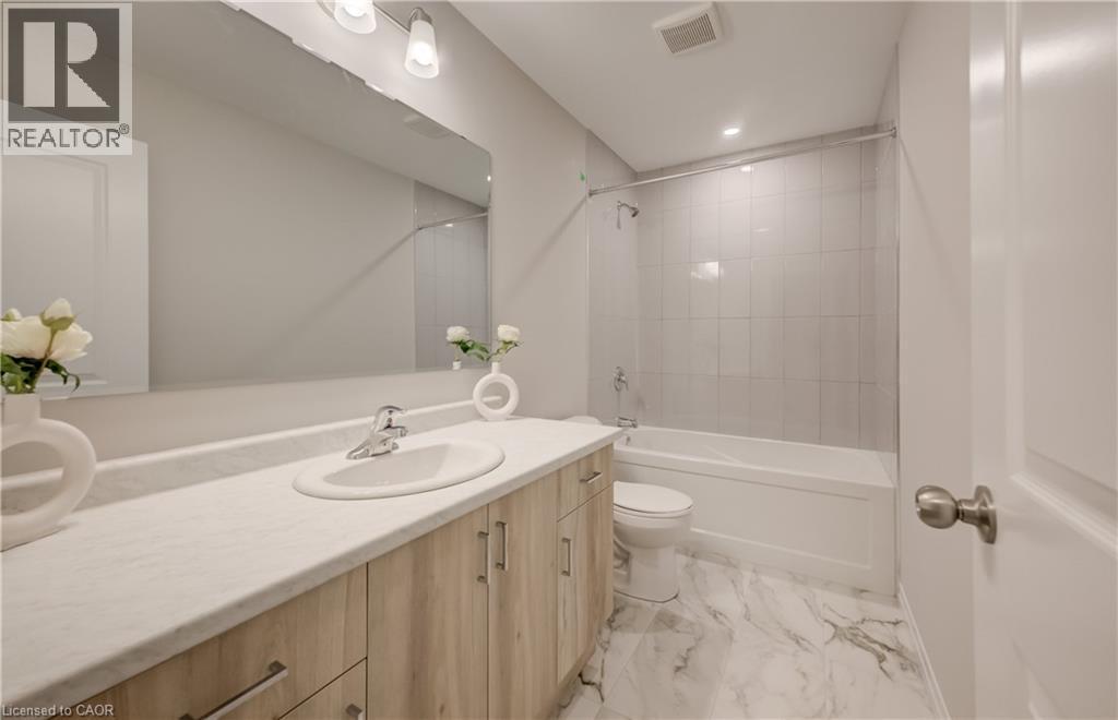 Bathroom featuring a wood-finish vanity with a light-toned countertop, an integrated sink, and a large wall-mounted mirror - 89 Rivergreen Crescent, Cambridge, ON - Indoor Photo Showing Bathroom