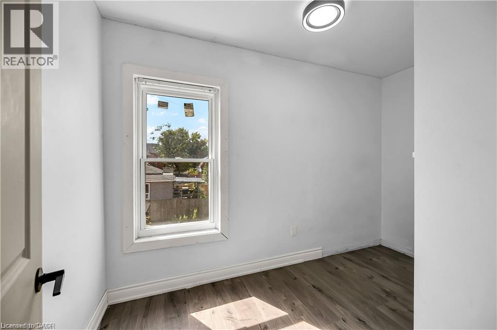 Bright secondary bedroom featuring a large casement window with white trim, wood-finish flooring, and recessed ceiling lighting - 334 Cannon Street E, Hamilton, ON - Indoor Photo Showing Other Room