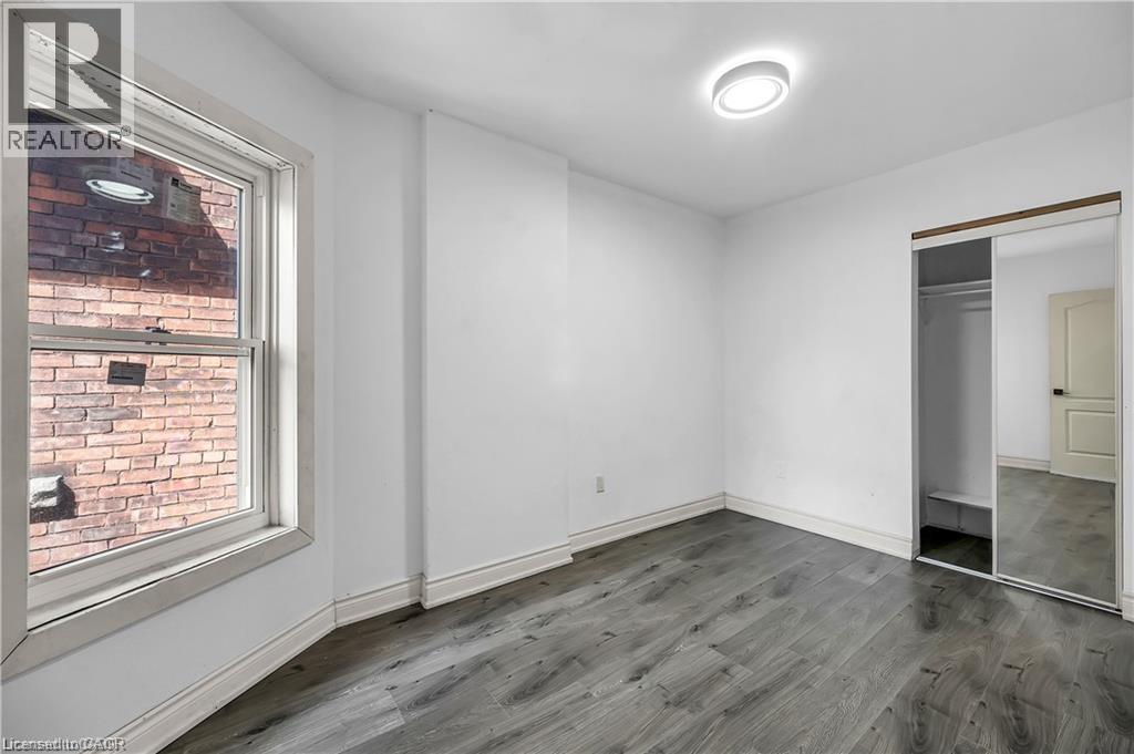 Spacious bedroom with wood-finish flooring, abundant natural light from large window with brick exterior views, mirrored closet doors, and recessed ceiling lighting - 334 Cannon Street E, Hamilton, ON - Indoor Photo Showing Other Room