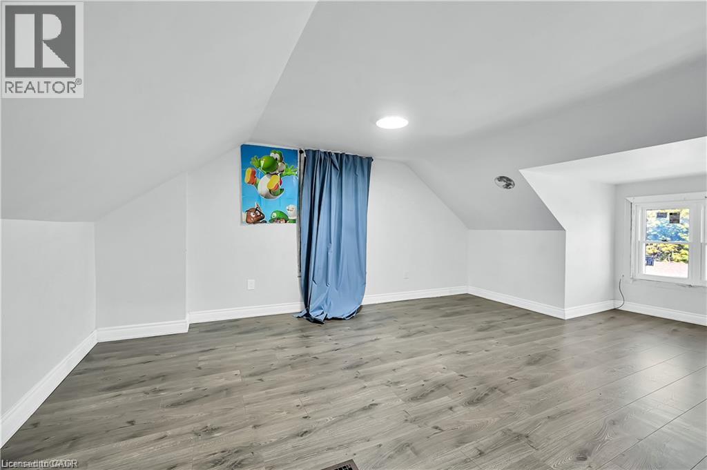 Spacious room featuring sloped ceilings, light gray wood-finish flooring, white baseboards, and a circular ceiling light fixture - 334 Cannon Street E, Hamilton, ON - Indoor Photo Showing Other Room