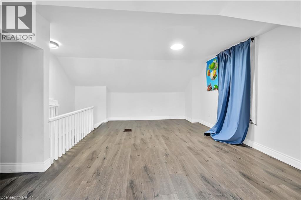 Spacious upper-level room featuring wood-finish flooring, a white spindle railing, and a window with blue drapes - 334 Cannon Street E, Hamilton, ON - Indoor