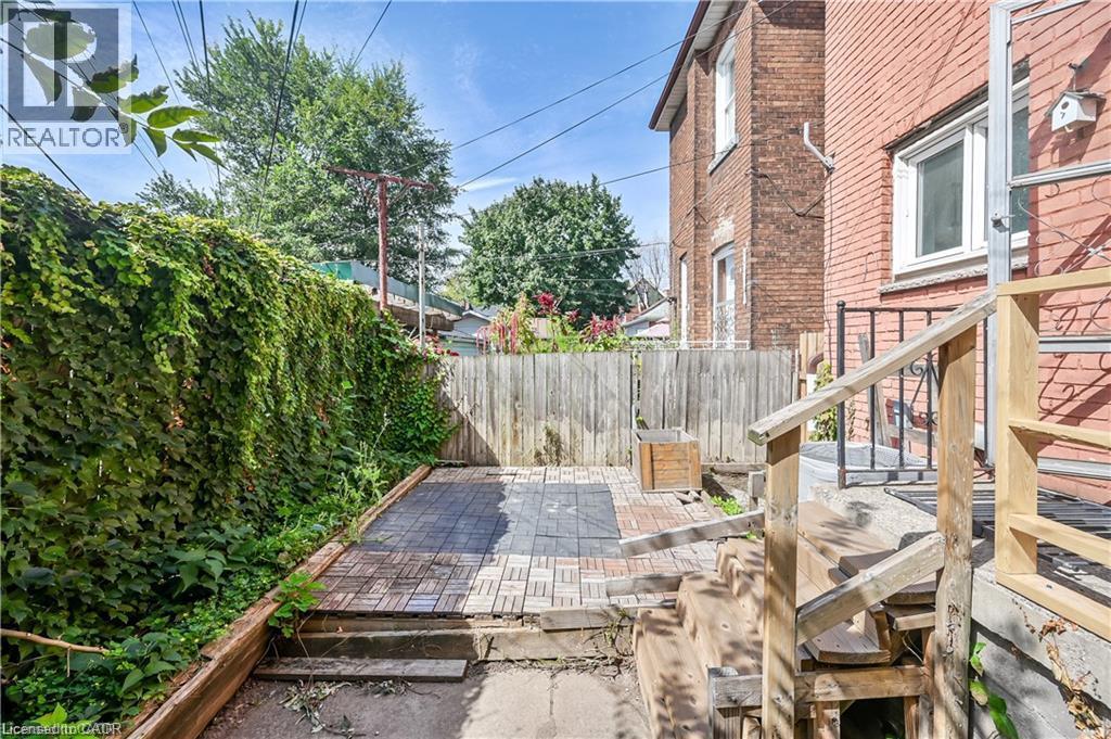 Spacious backyard retreat featuring a composite deck with integrated seating areas, mature privacy hedging along the perimeter, wooden fence enclosure, and mature shade trees - 334 Cannon Street E, Hamilton, ON - Outdoor