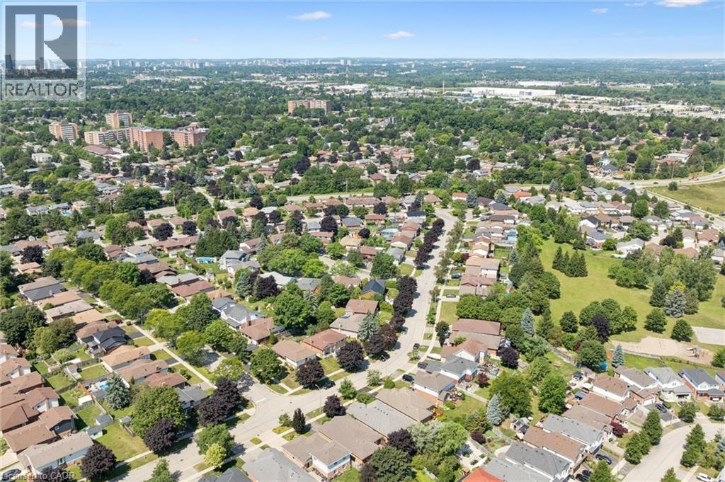 Expansive aerial encompassing a residential neighborhood with detached homes, mature tree coverage, clear skies, visible streets, and distant city structures - 187 Westchester Drive, Kitchener, ON - Outdoor With View