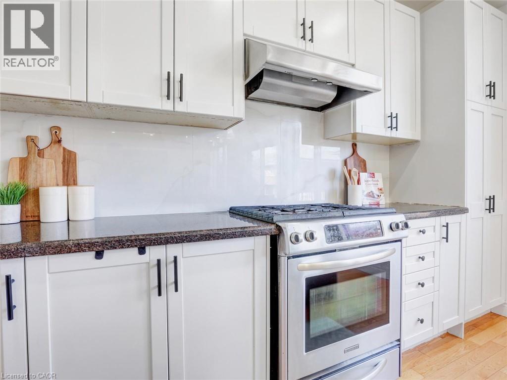 Kitchen featuring white shaker-style cabinetry with black hardware, a stainless steel range and oven, a stainless steel range hood, stone countertops, and a full-height backsplash - 584 Pinery Trail, Waterloo, ON - Indoor Photo Showing Kitchen With Upgraded Kitchen