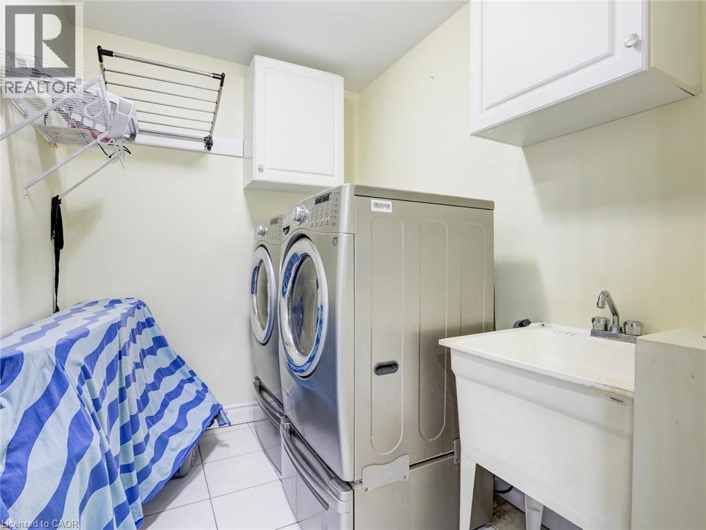 Dedicated laundry area featuring a utility sink, white wall-mounted cabinetry, and tiled flooring - 584 Pinery Trail, Waterloo, ON - Indoor Photo Showing Laundry Room