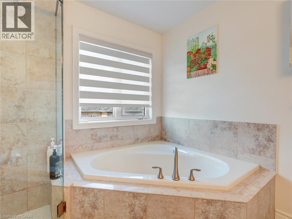 Corner soaking tub with deck-mounted brushed nickel fixtures, surrounded by neutral-toned tile and a glass-enclosed shower - 584 Pinery Trail, Waterloo, ON - Indoor Photo Showing Bathroom