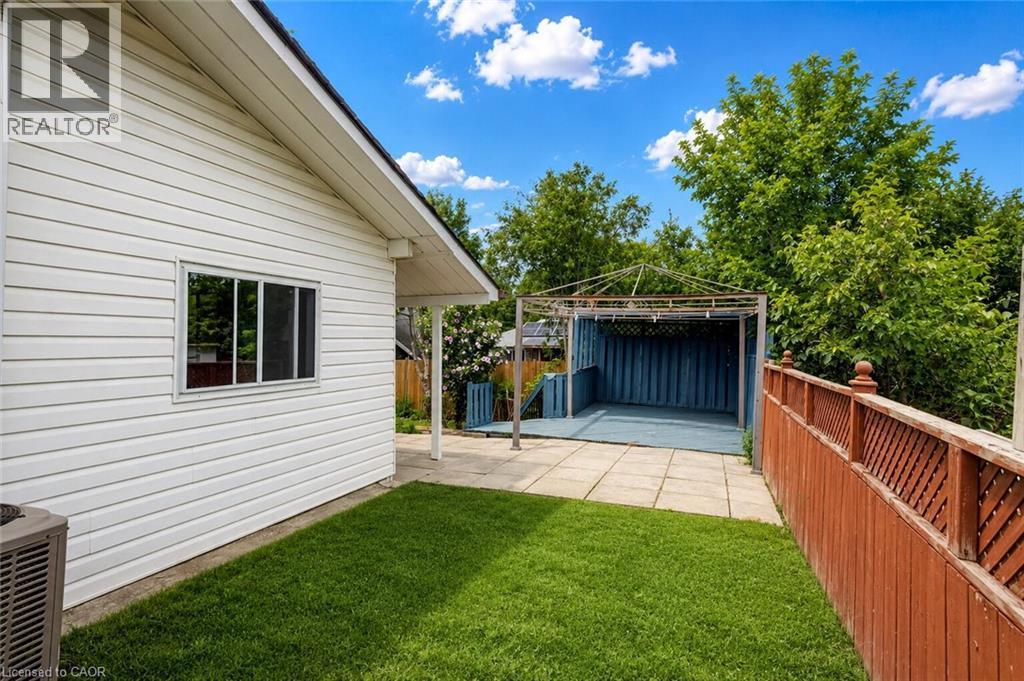 Rear exterior featuring white horizontal siding, a covered patio area with a blue floor, a metal frame structure, a wood privacy fence, and a manicured lawn - 182 Avalon Place, Kitchener, ON - Outdoor With Exterior
