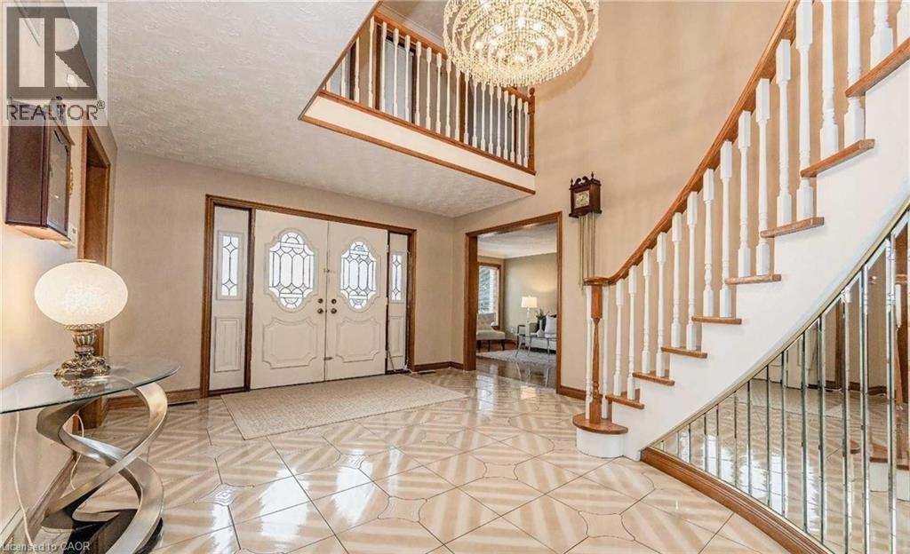 Grand foyer featuring double entry doors with decorative glass, a curved staircase with wood treads and white balusters, an upper-level balcony, and a multi-tiered chandelier - 28 Walnut Drive, Guelph, ON - Indoor Photo Showing Other Room