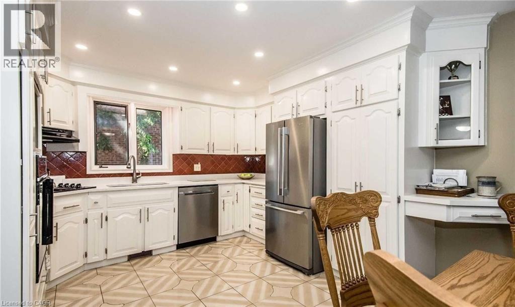 White cabinetry with crown molding, stainless steel appliances, a tile backsplash, recessed lighting, and a built-in desk area - 28 Walnut Drive, Guelph, ON - Indoor Photo Showing Kitchen