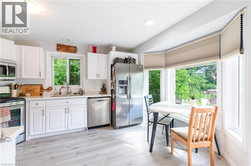 Kitchen featuring bright white cabinetry, stainless steel appliances, light wood-finish flooring, a mosaic tile backsplash, and a bay window with pleated shades - 907 Doon Village Road, Kitchener, ON - Indoor Photo Showing Kitchen