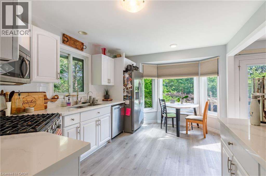 Bright, open kitchen and dining area featuring white cabinetry, gas cooktop, stainless steel appliances, quartz countertops, and abundant natural light from multiple window banks - 907 Doon Village Road, Kitchener, ON - Indoor Photo Showing Kitchen With Double Sink