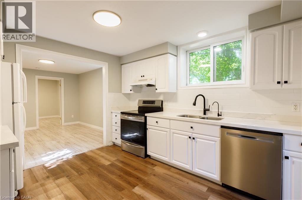 Renovated kitchen featuring white cabinetry, light-colored countertops, stainless steel appliances, a black matte faucet, and wood-finish flooring - 907 Doon Village Road, Kitchener, ON - Indoor Photo Showing Kitchen With Double Sink