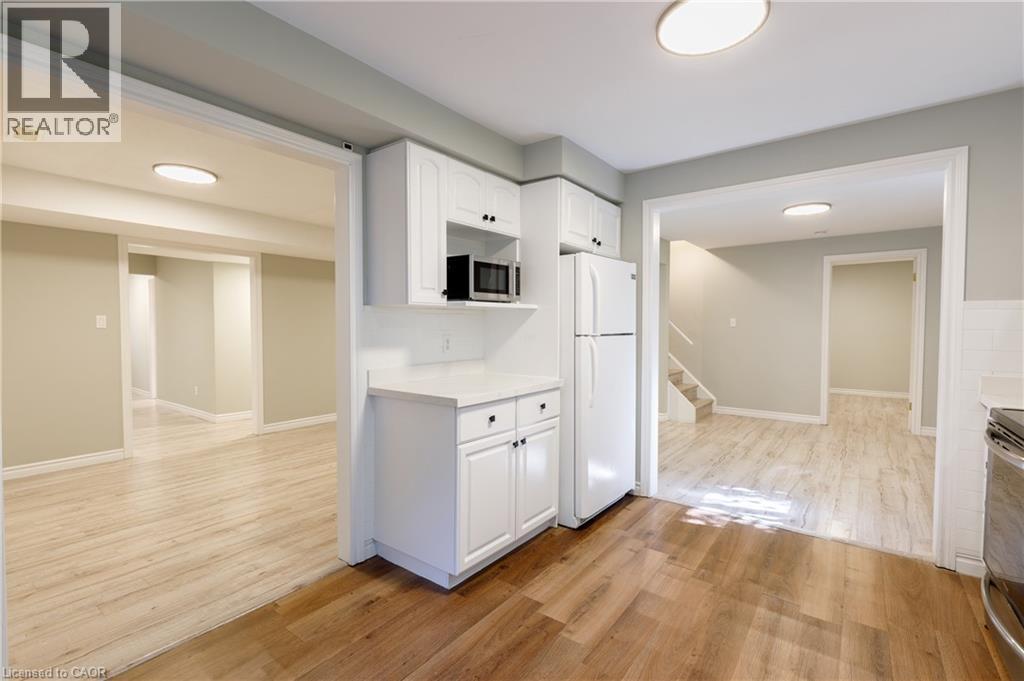 Bright, open-concept living space featuring wood-finish flooring throughout, recessed ceiling lighting, and white cabinetry with stainless steel appliances - 907 Doon Village Road, Kitchener, ON - Indoor Photo Showing Other Room