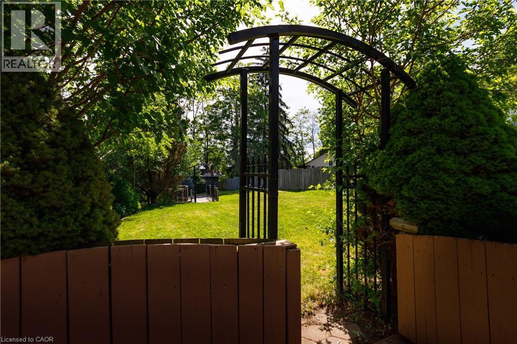 Expansive backyard featuring a lush lawn, mature trees, and a decorative metal archway with a gate - 907 Doon Village Road, Kitchener, ON - Outdoor