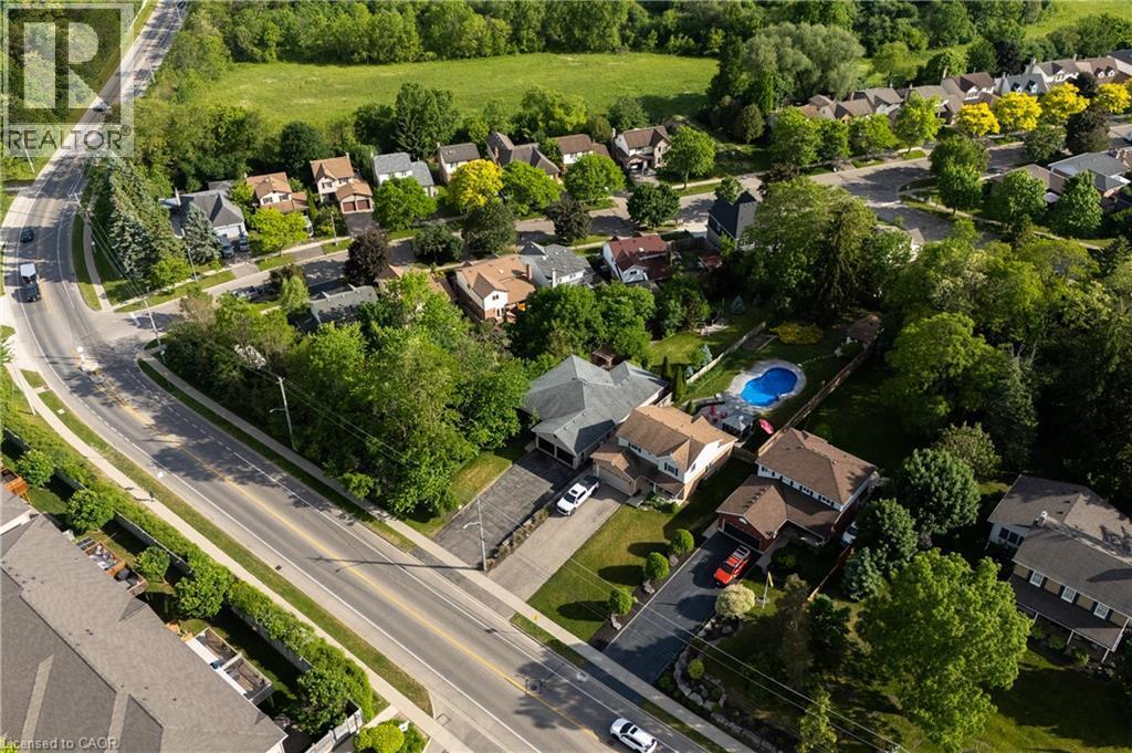 Aerial view of this residential estate showcasing a sprawling manicured lawn, mature tree-lined landscaping, in-ground swimming pool with surrounding hardscape, multi-car driveway, and substantial bri - 907 Doon Village Road, Kitchener, ON - Outdoor With View