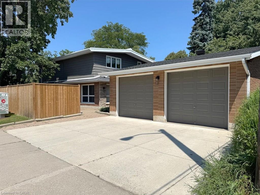 Exterior featuring a two-car garage with three panel doors, brick and stone accents, and dark siding - 69 Pleasant Avenue, Hamilton, ON - Outdoor