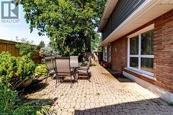 Paver patio featuring brick exterior, white window trim, and established landscaping - 