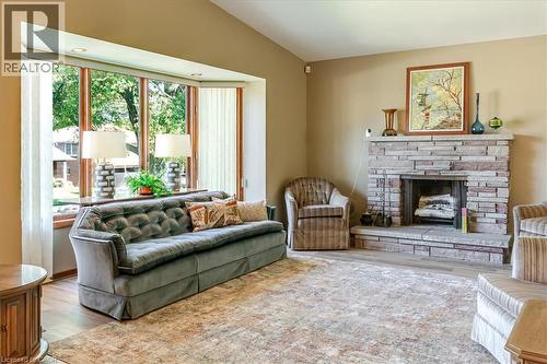 Spacious living area featuring a stone-clad fireplace with hearth, a prominent bay window, and light wood-finish flooring - 69 Pleasant Avenue, Hamilton, ON - Indoor Photo Showing Living Room With Fireplace
