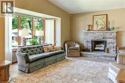 Spacious living area featuring a stone-clad fireplace with hearth, a prominent bay window, and light wood-finish flooring - 