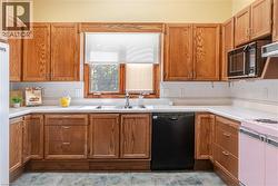 Kitchen featuring wood cabinetry, white countertops, tile backsplash, stainless steel sink with chrome faucet, and a window with natural light - 