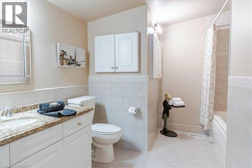 Bathroom featuring a single vanity with a granite-patterned countertop, a built-in tub with shower, and light-toned tile flooring - 69 Pleasant Avenue, Hamilton, ON - Indoor Photo Showing Bathroom